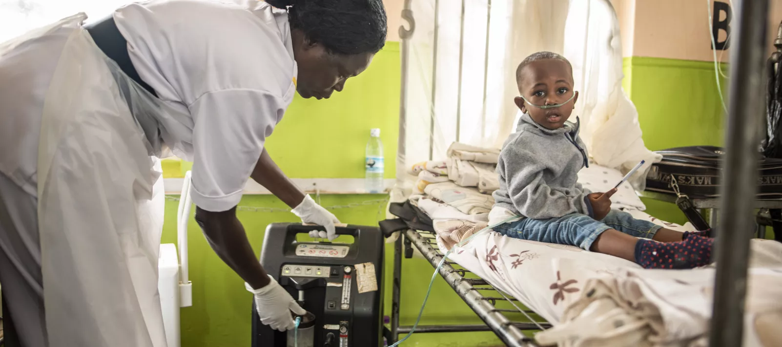 A nurse adjusts a portable oxygen concentrator machine to administer oxygen to a child to treat severe pneumonia