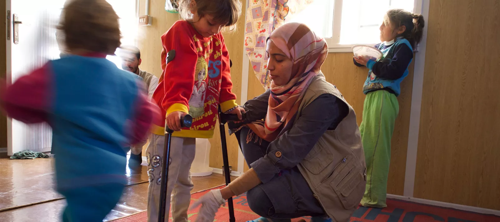 A physiotherapist helps a young girl practise walking with crutches 