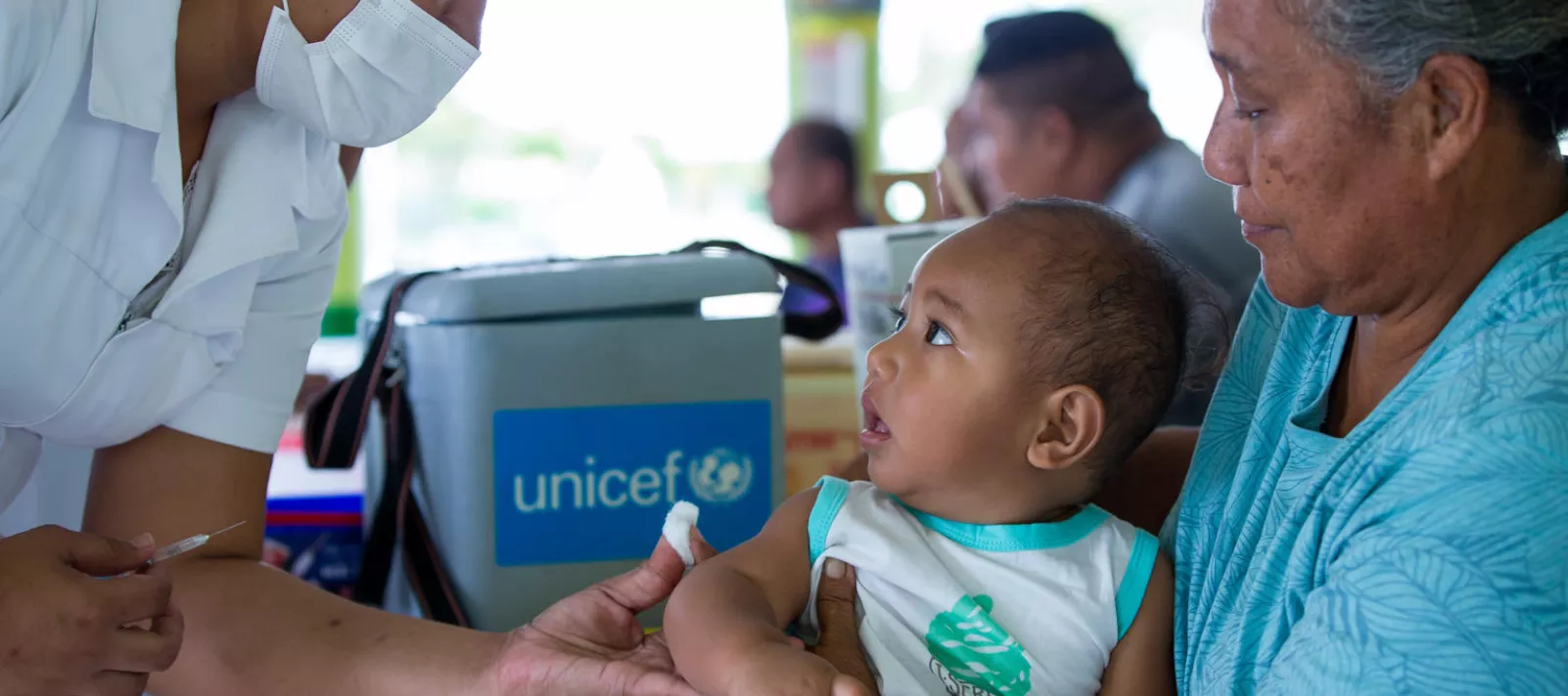 A nurse vaccinates a baby who is sitting on his grandmother's lap 