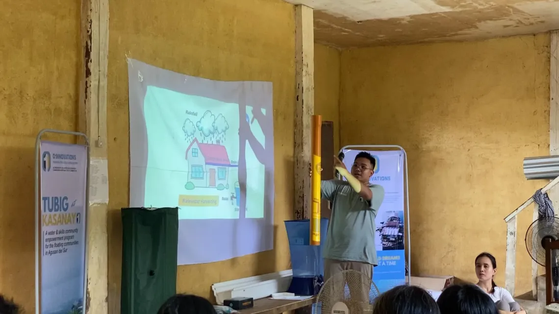 A man demonstrates rain water harvesting and filtration system to an audience using a projector