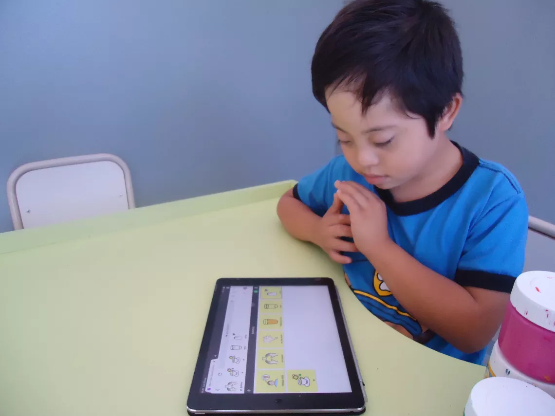 A child learns how to communicate and express his needs using AAC application Cboard.