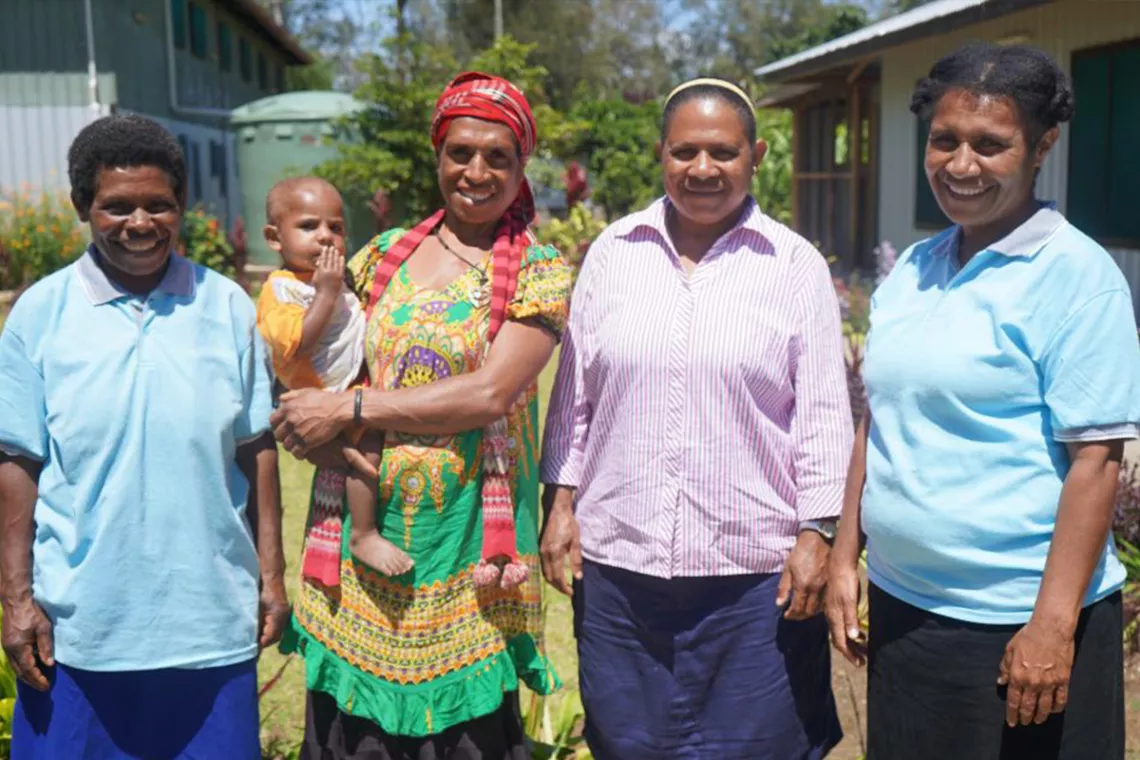 Four women - one of them holding a baby - pose for the camera 