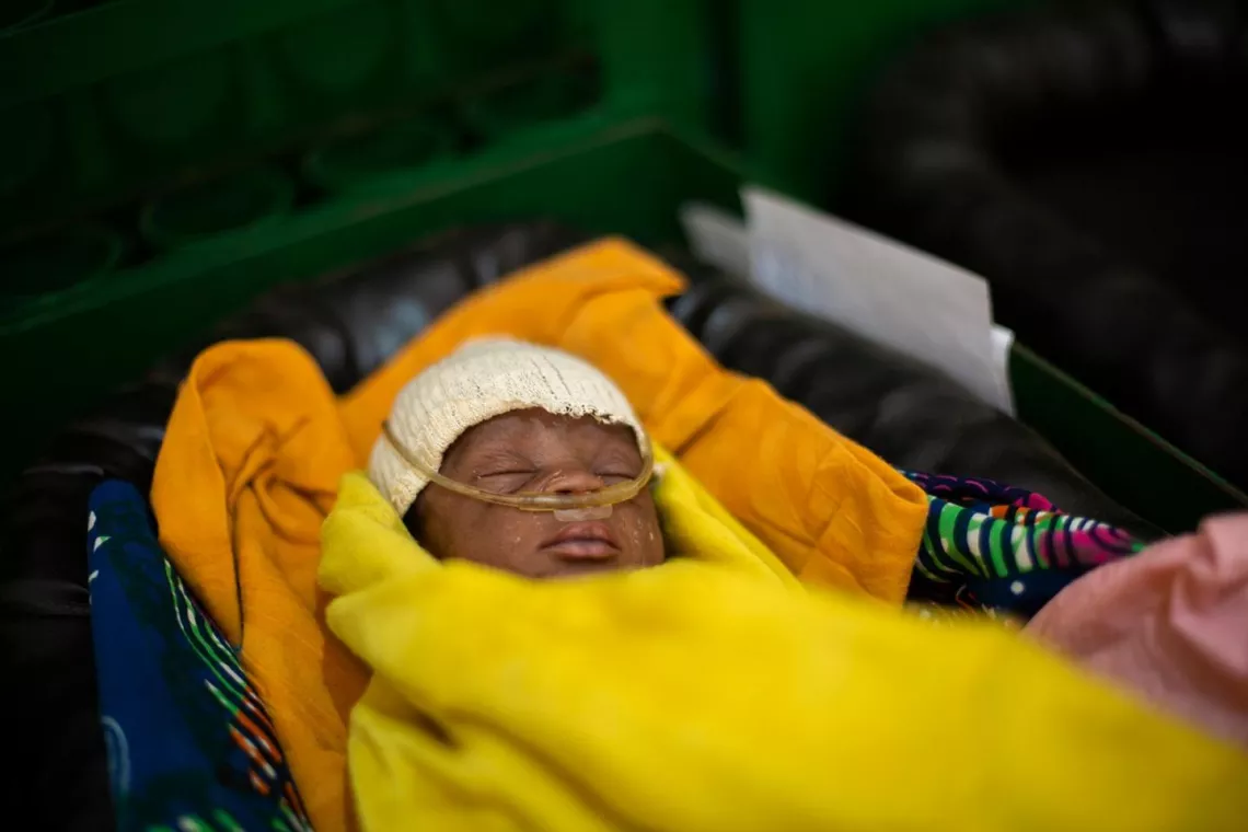 A baby wrapped in a yellow blanket receives oxygen via a nasal cannula
