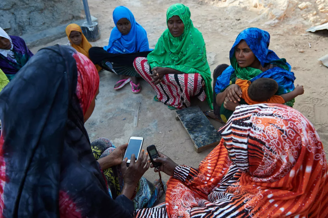 During a group meeting, Father Idleh, Marketing In-charge - Income Generation Committee, show women how to market their products using mobile phone, in the village of Assamo in Djibouti.