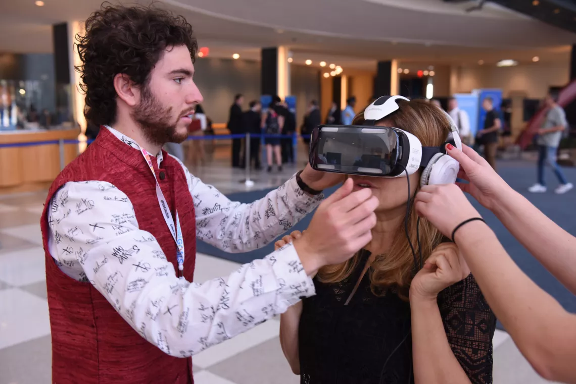 Sustainable Development Goals (SDG) Action Campaign Consultant Alex Samaras (left) assists UNICEF Division of Communication Director Paloma Escudero with a virtual reality (VR) headset at United Nations Headquarters. The headset allows the user to view three-dimensional videos that have been made to demonstrate the global development challenges of humanitarian crises.