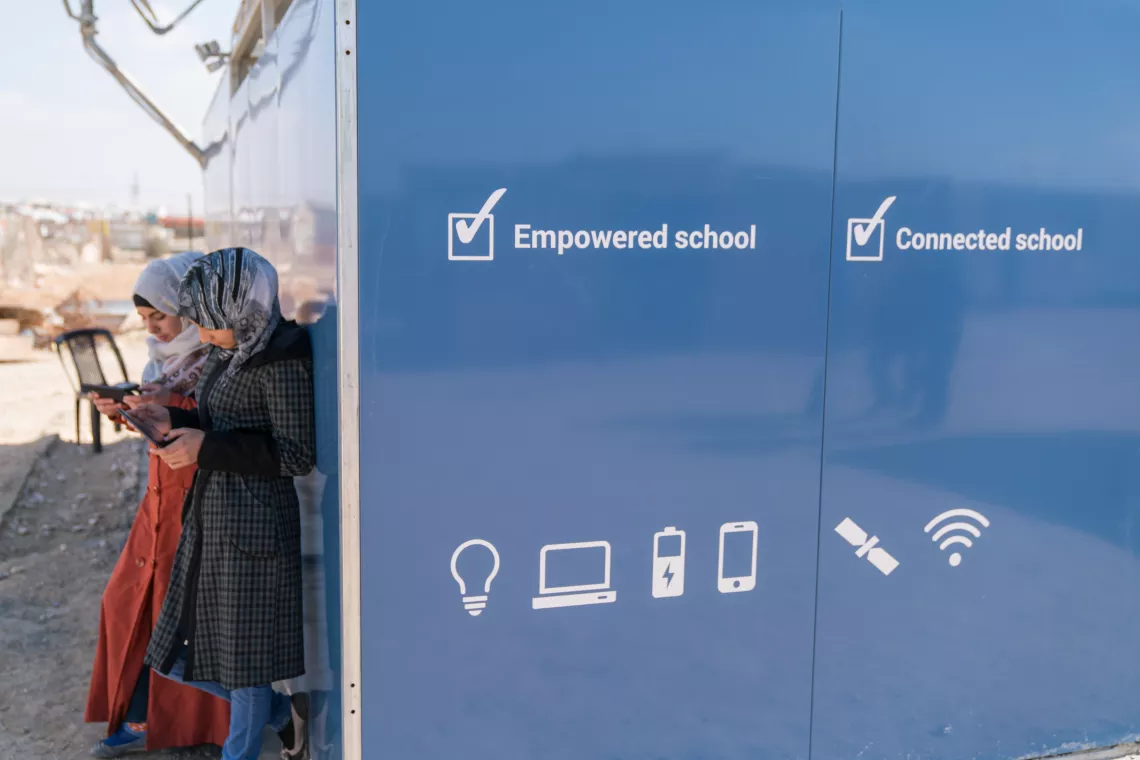 in Jordan, two adolescent girls use cellphones outside a solar kiosk in the Za&rsquo;atari camp for Syrian refugees