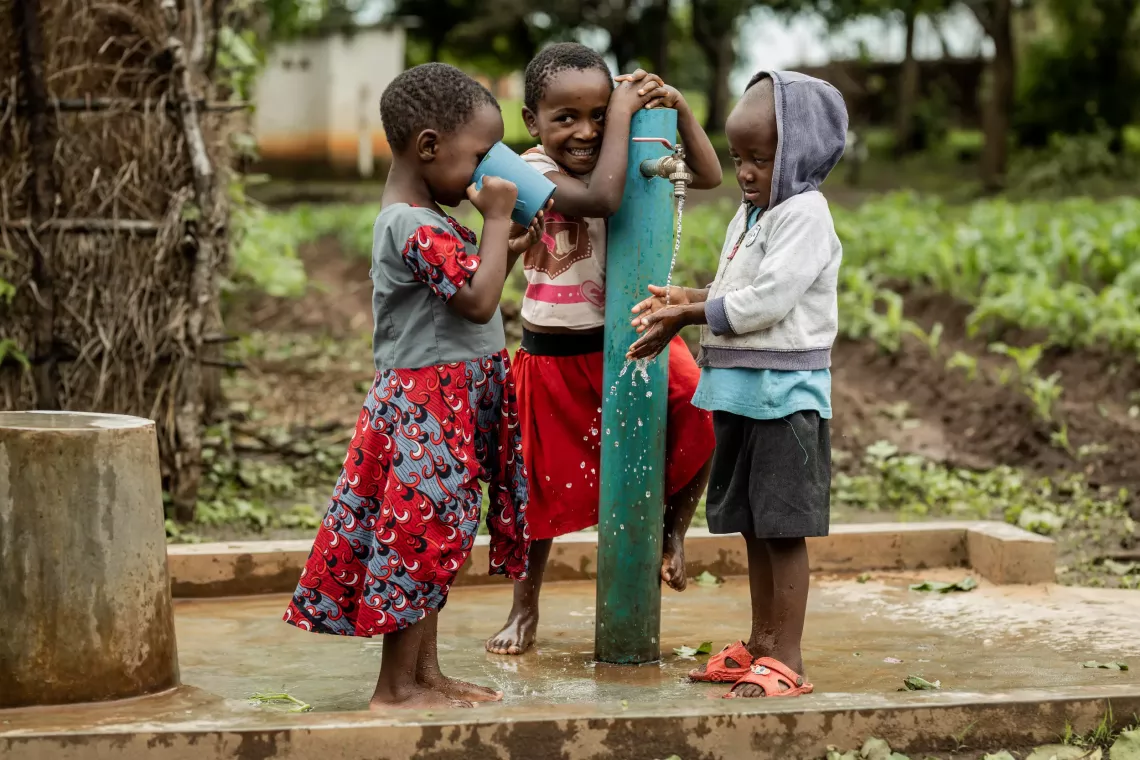 Three children smile as they wash their hands