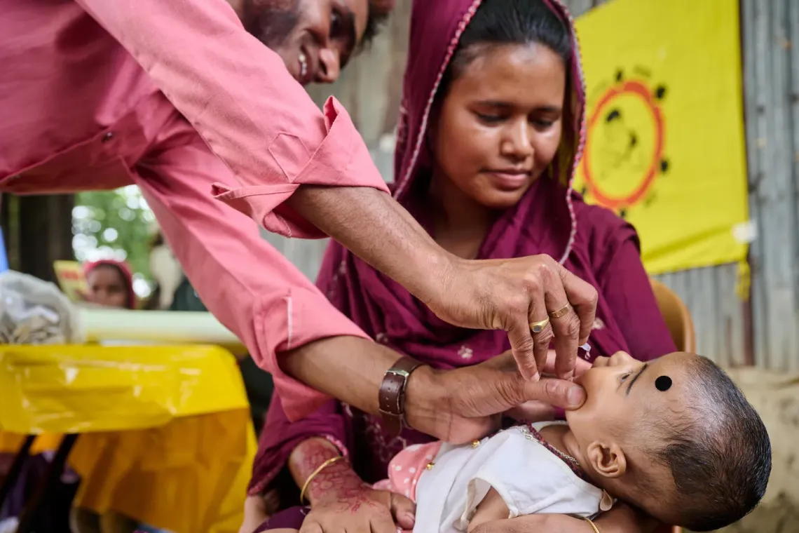 Vaccinator Abdul Baten administers a polio vaccine dose to an infant