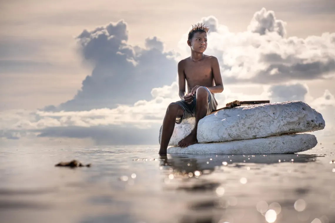 A boy sits on a makeshift raft at a beach in Tarawa, Kiribati. 
