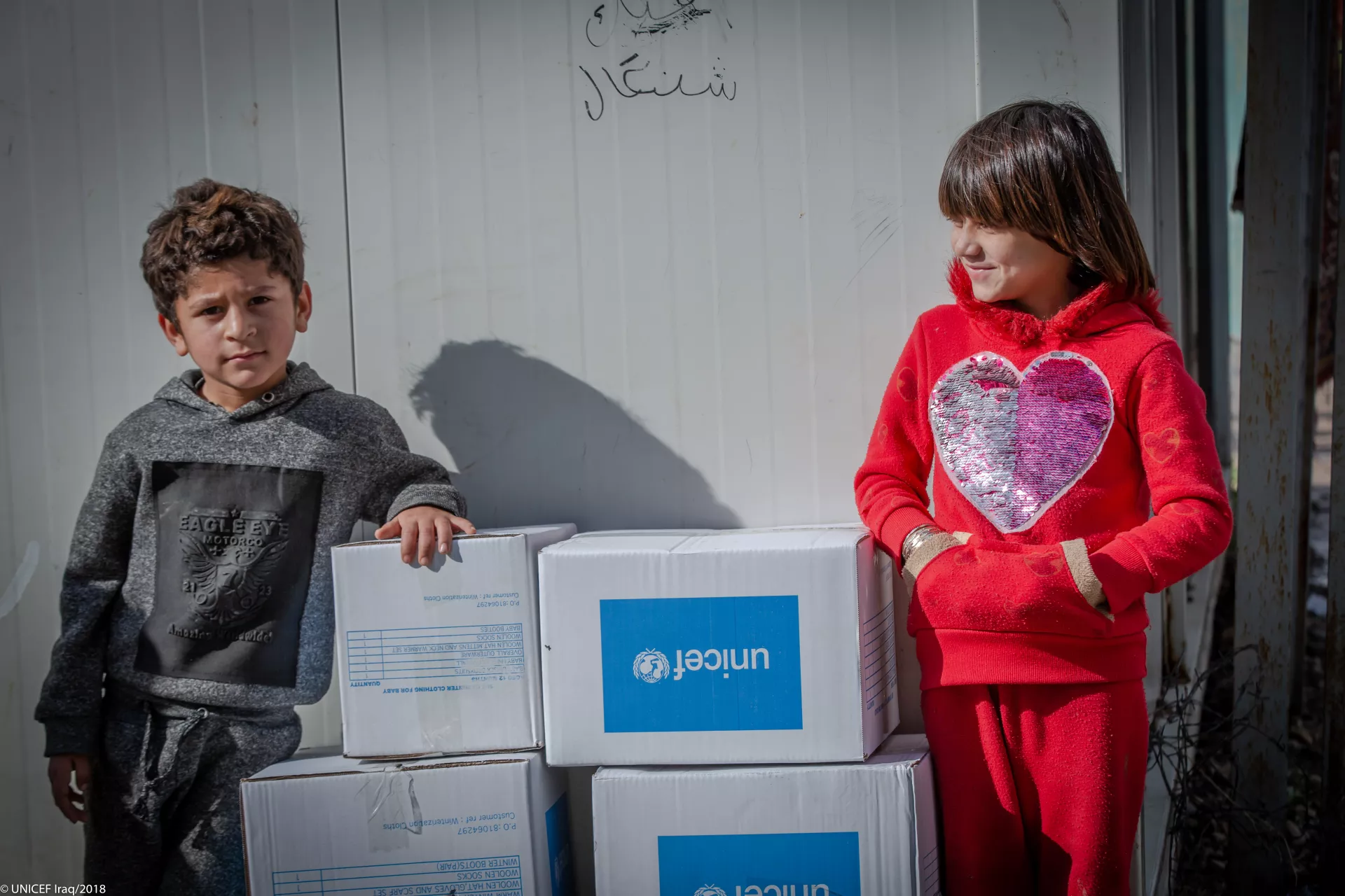 A brother and a sister are standing beside UNICEF kits