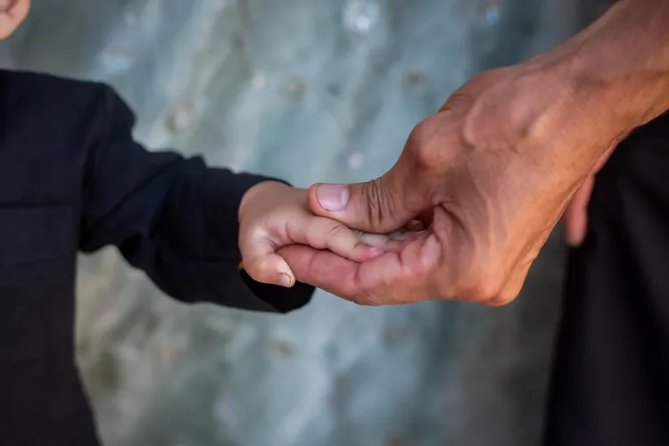 Adult hand gently holding a child's hand against a blurred background, suggesting care and support.