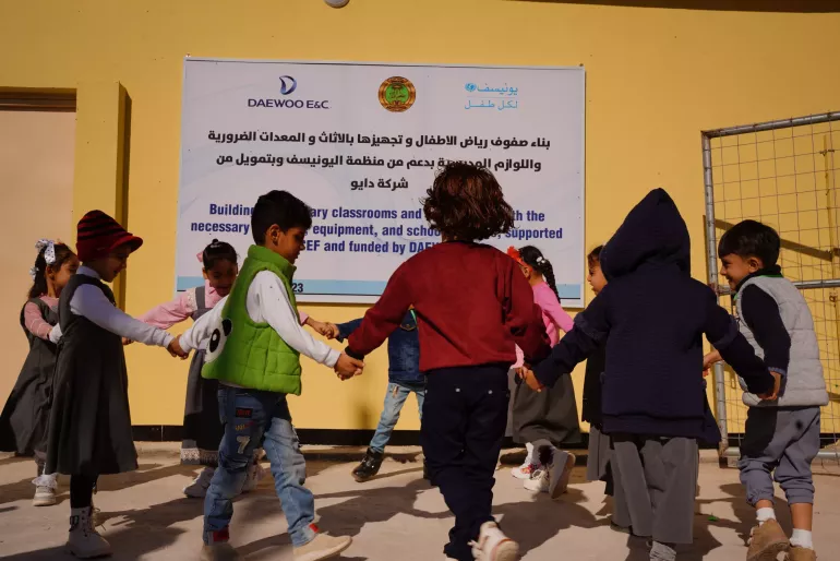 Children are playing in front of the banner hanging on the wall outside of the ECE class in 14 Athar Primary School.