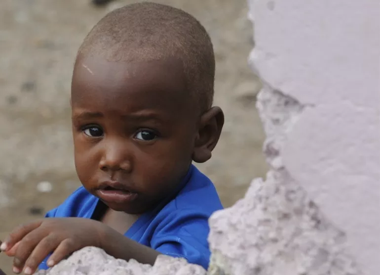 Photograph of a child standing behind a wall
