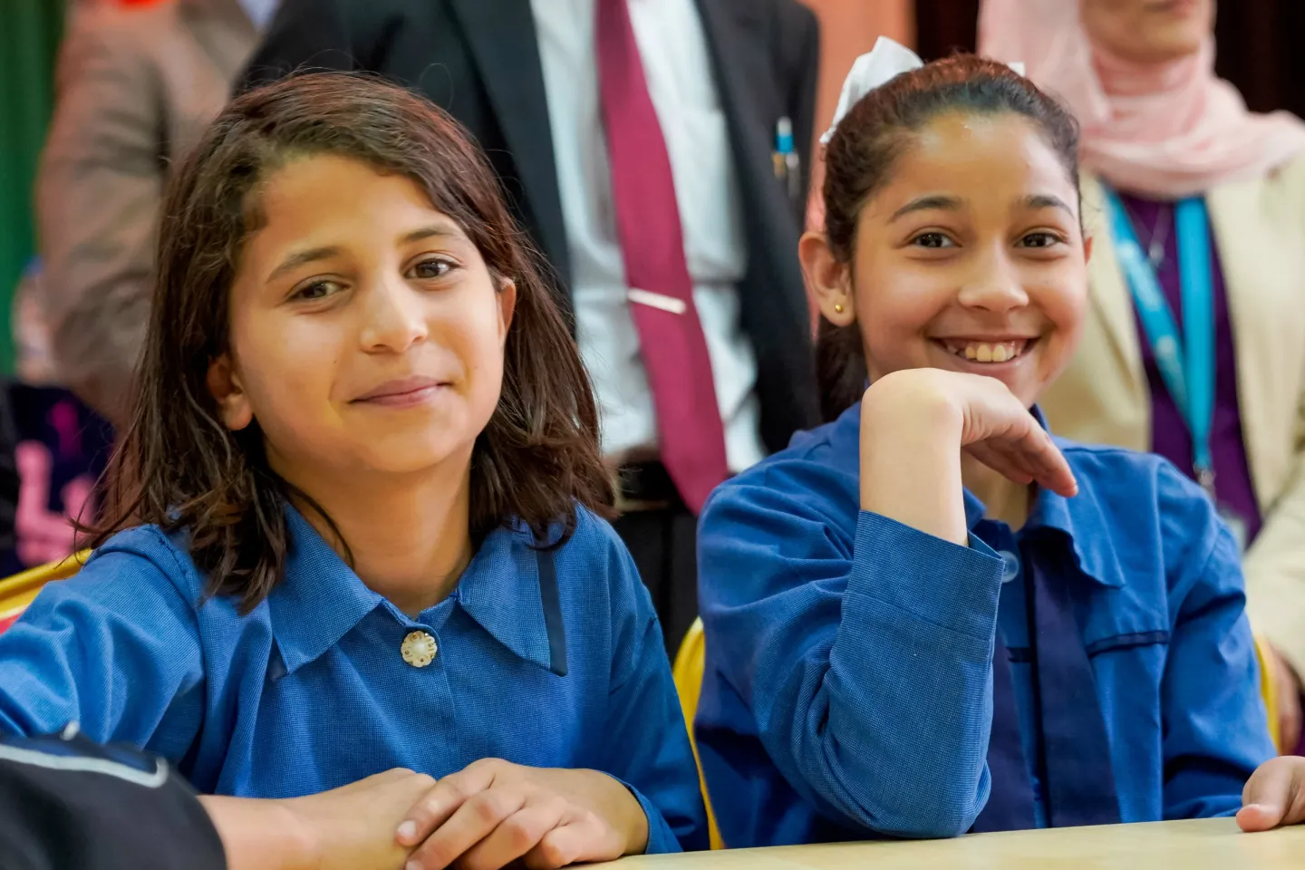 Two girls in school uniforms sit next to one another