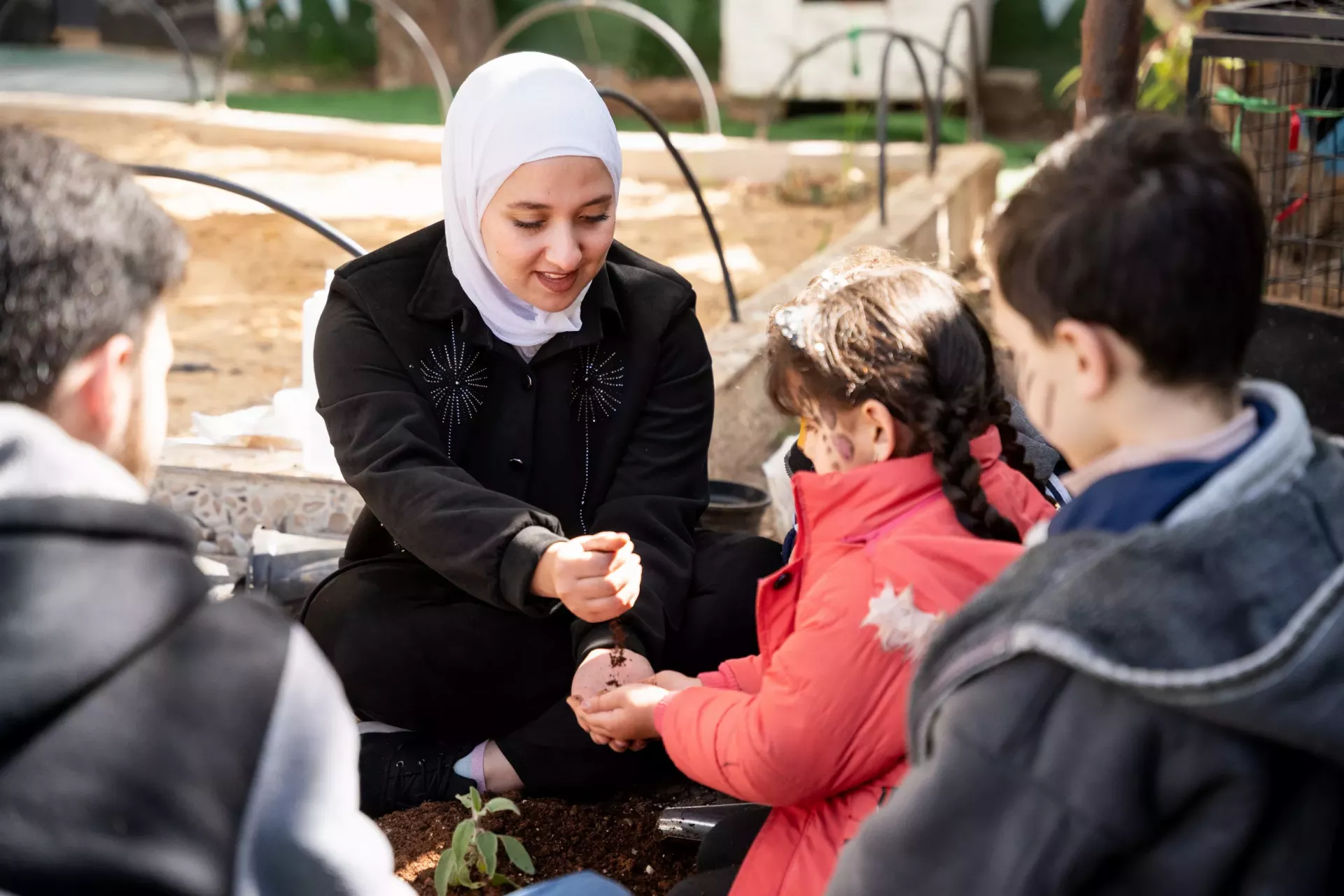Kids sitting around a woman planting.