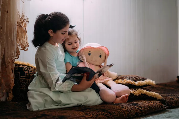 Ghofran, 12, reads to her little sister Noor, 4, at home in Za'atari refugee camp. 