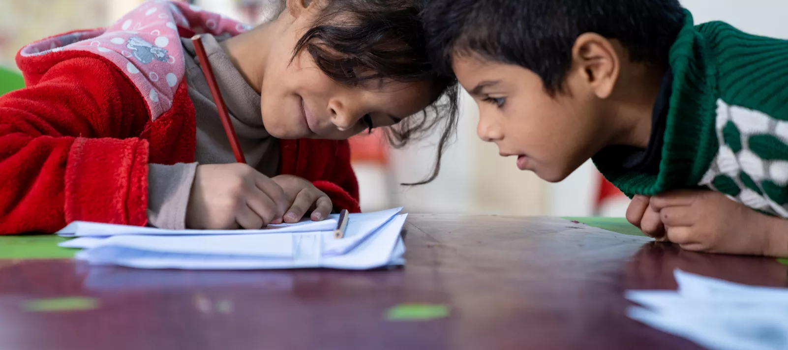 A girl writes in a notebook while a boy looks on