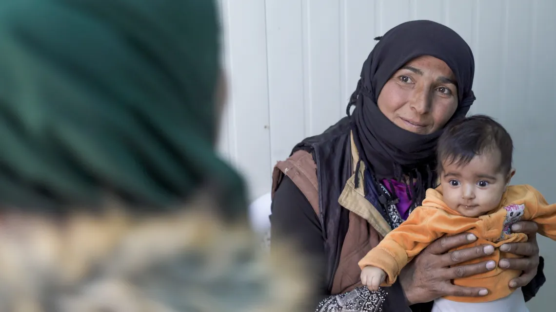 A woman holds her baby facing another woman