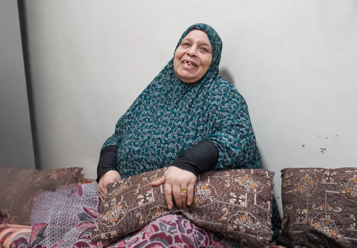 A woman sitting on a mattress on the ground inside her home. 