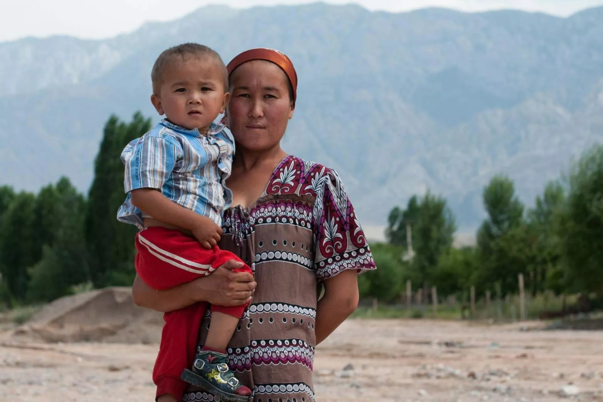 A mother holds her son in her arms against a mountainous backdrop