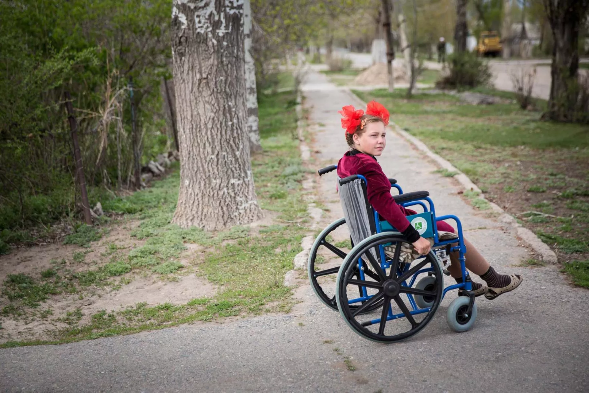 A girl in a wheelchair on a tree-lined sidewalk