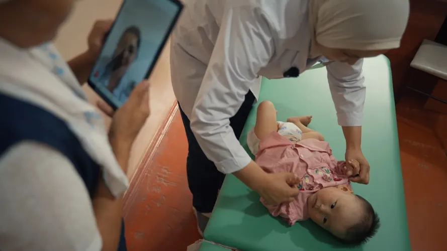 While the doctor examines the girl, the nurse demonstrates the entire process to another doctor via video call