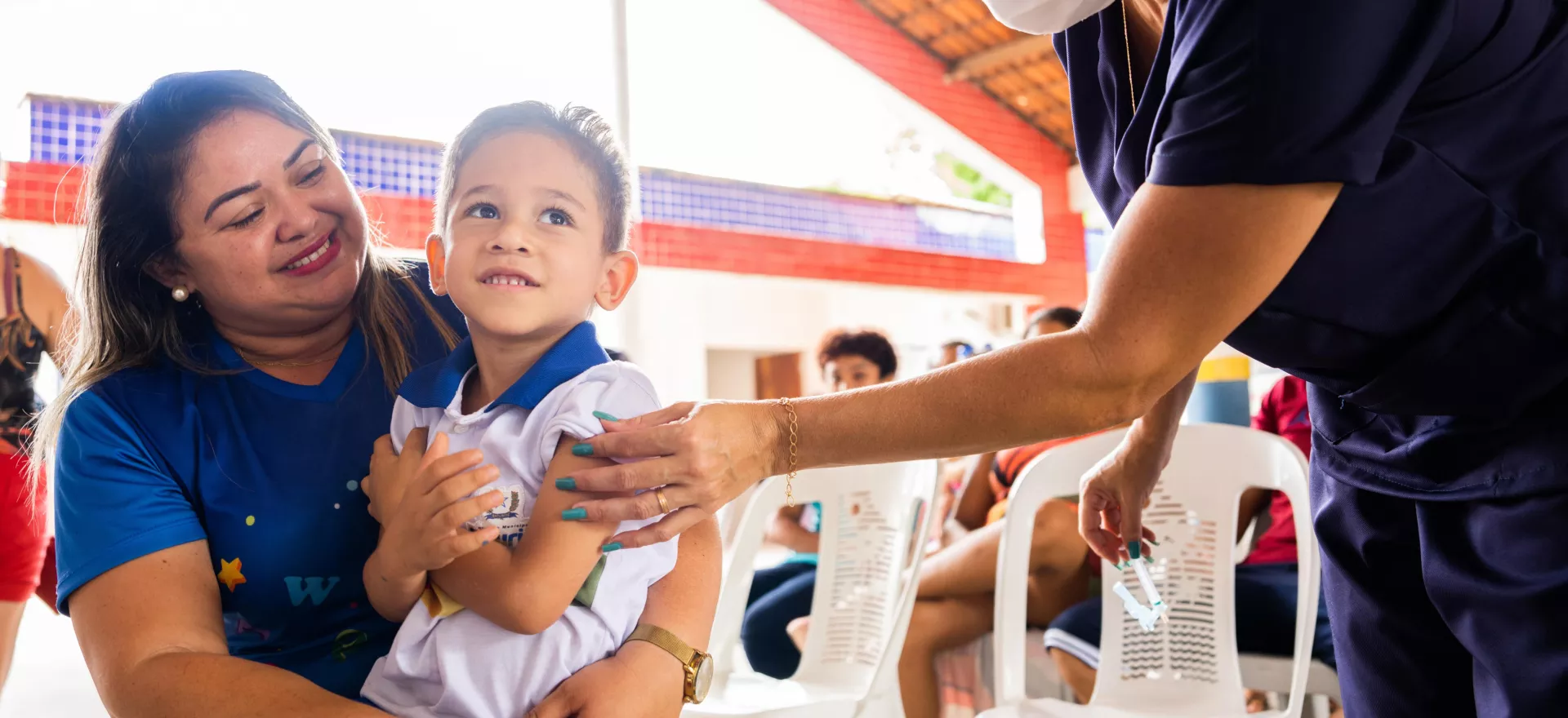 A young boy held by his mother receives a vaccination in his arm.