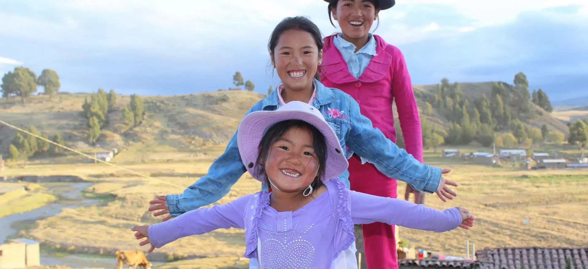 tres ni&ntilde;as sonriendo con los brazos extendidos frente a un campo