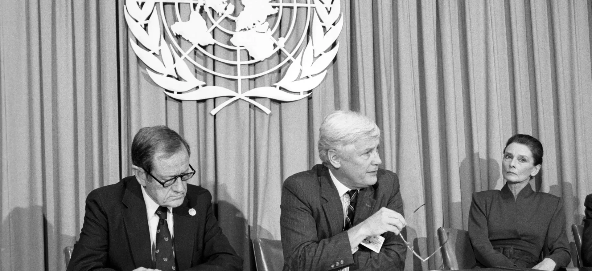 Dos hombres y una mujer sentados en una mesa con el logo de Naciones Unidas detr&aacute;s.