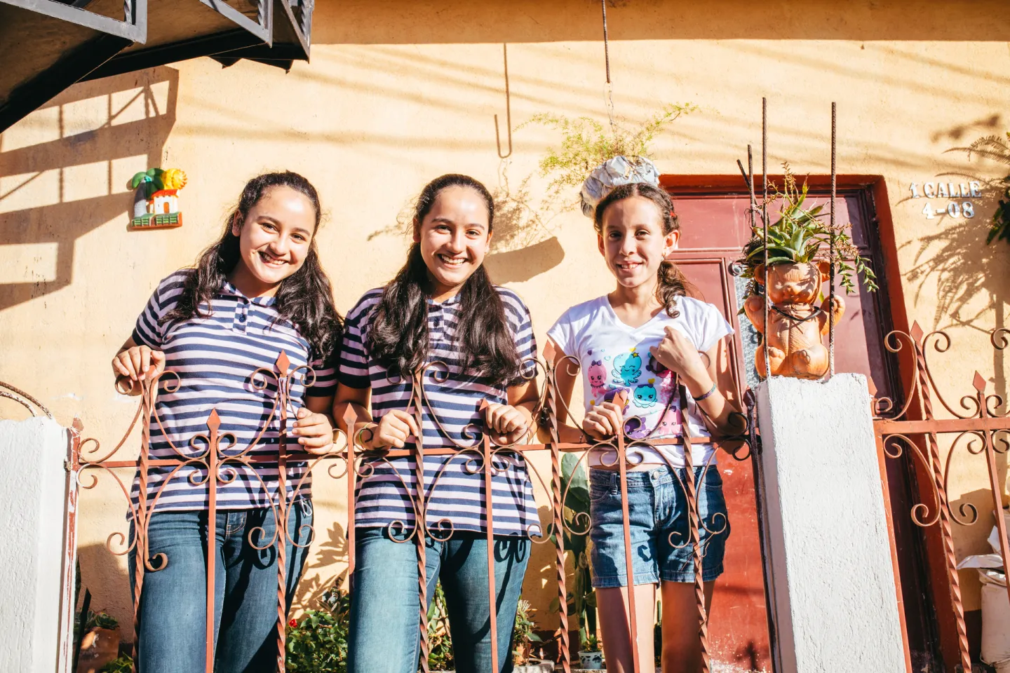Tres ni&ntilde;as sonriendo en la puerta de su casa.