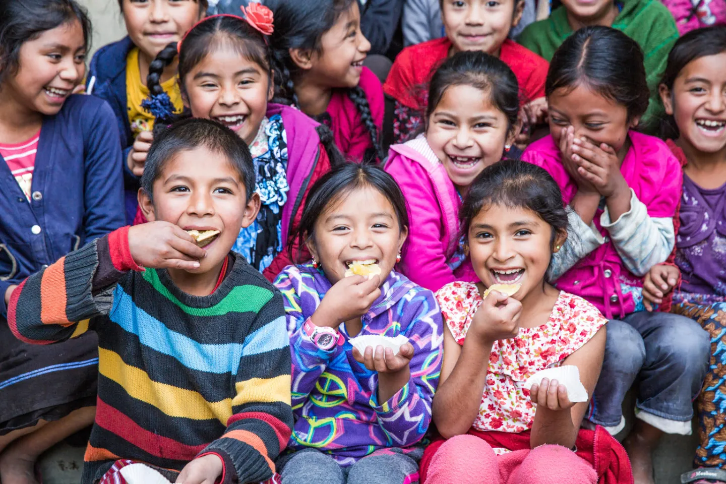 Grupo de ni&ntilde;os y ni&ntilde;as riendo y algunos comiendo galletas.