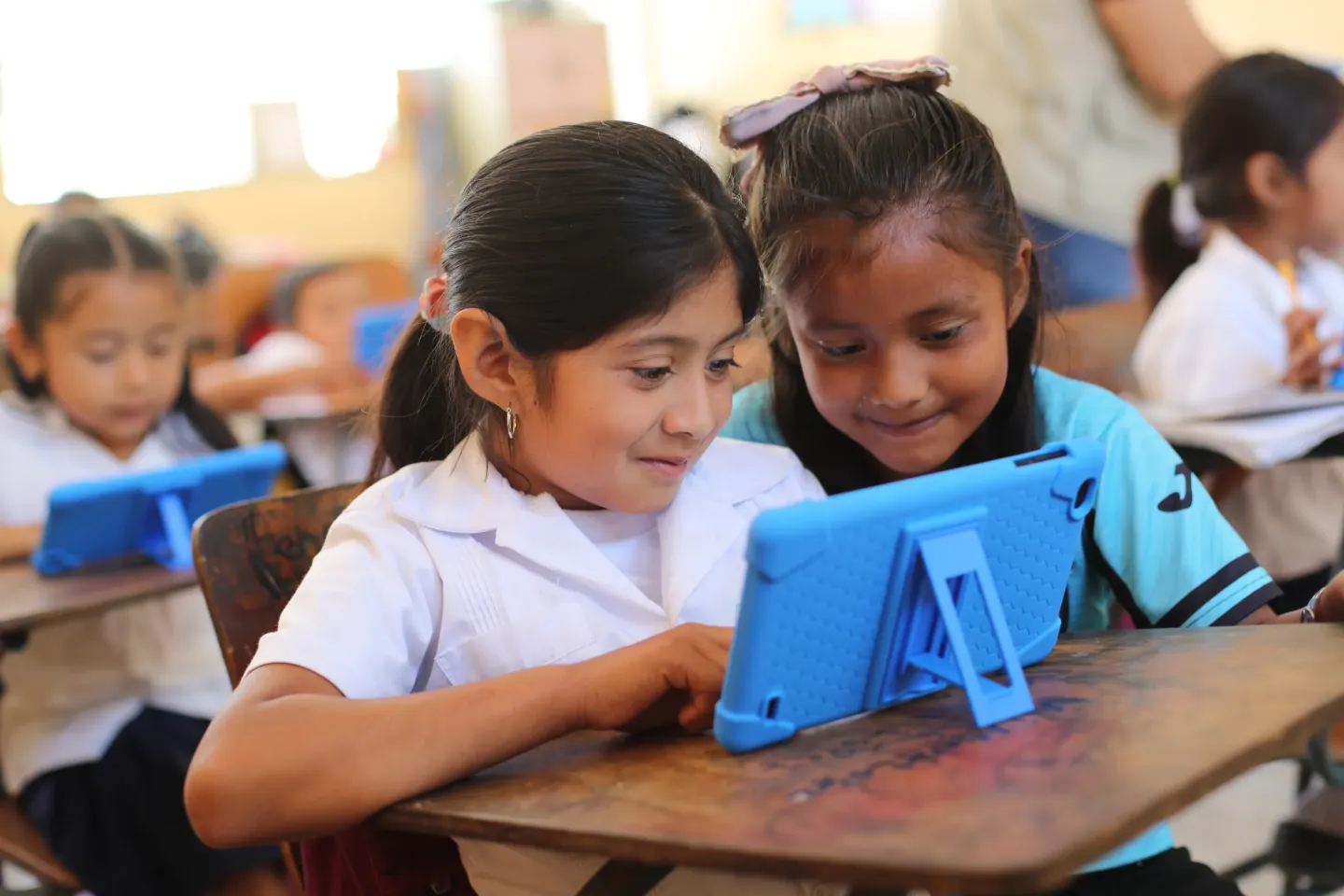 Dos ni&ntilde;as en un sal&oacute;n de clases viendo una tablet 
