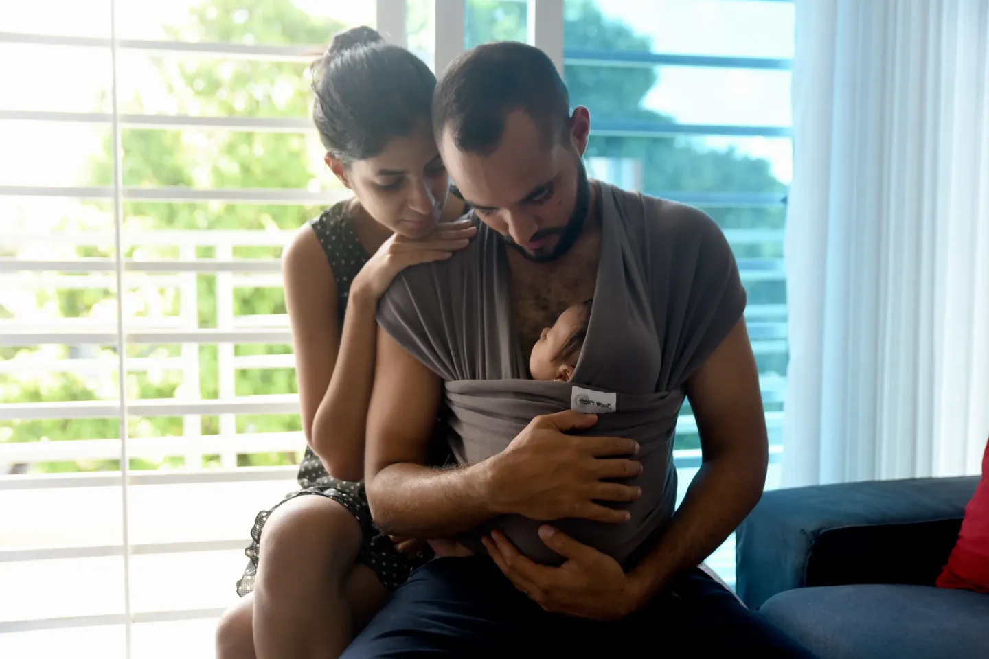 Un hombre y una mujer sentados, viendo a un bebe que es cargado por el hombre