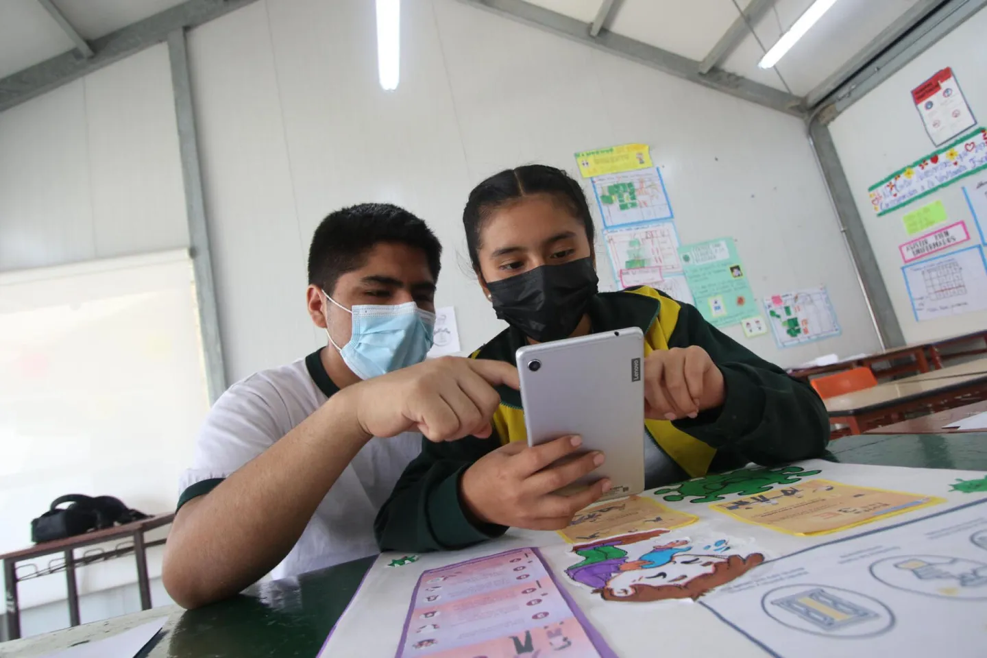 Dos jovenes miran un tablet en el salon de clases