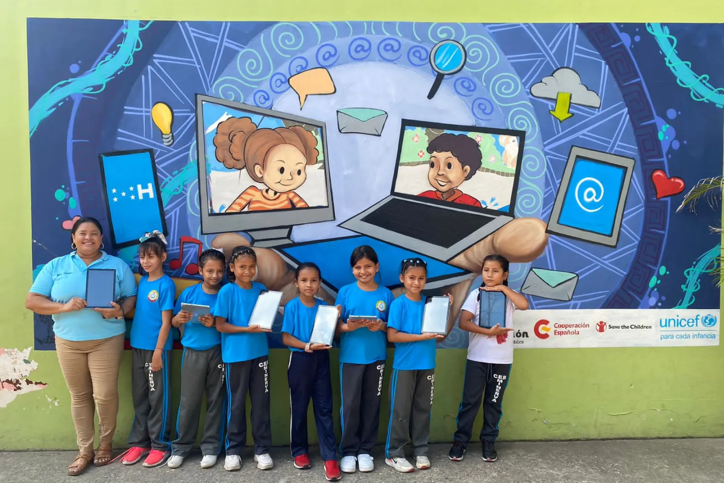 Un grupo de ni&ntilde;as con su maestra posan con sus tablets frente a un mural 