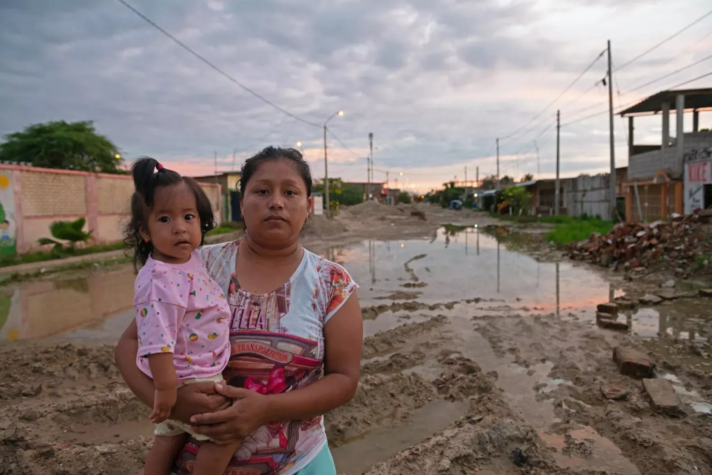 Una madfre sostiene a su hija peque&ntilde;a frente a una calle destruida