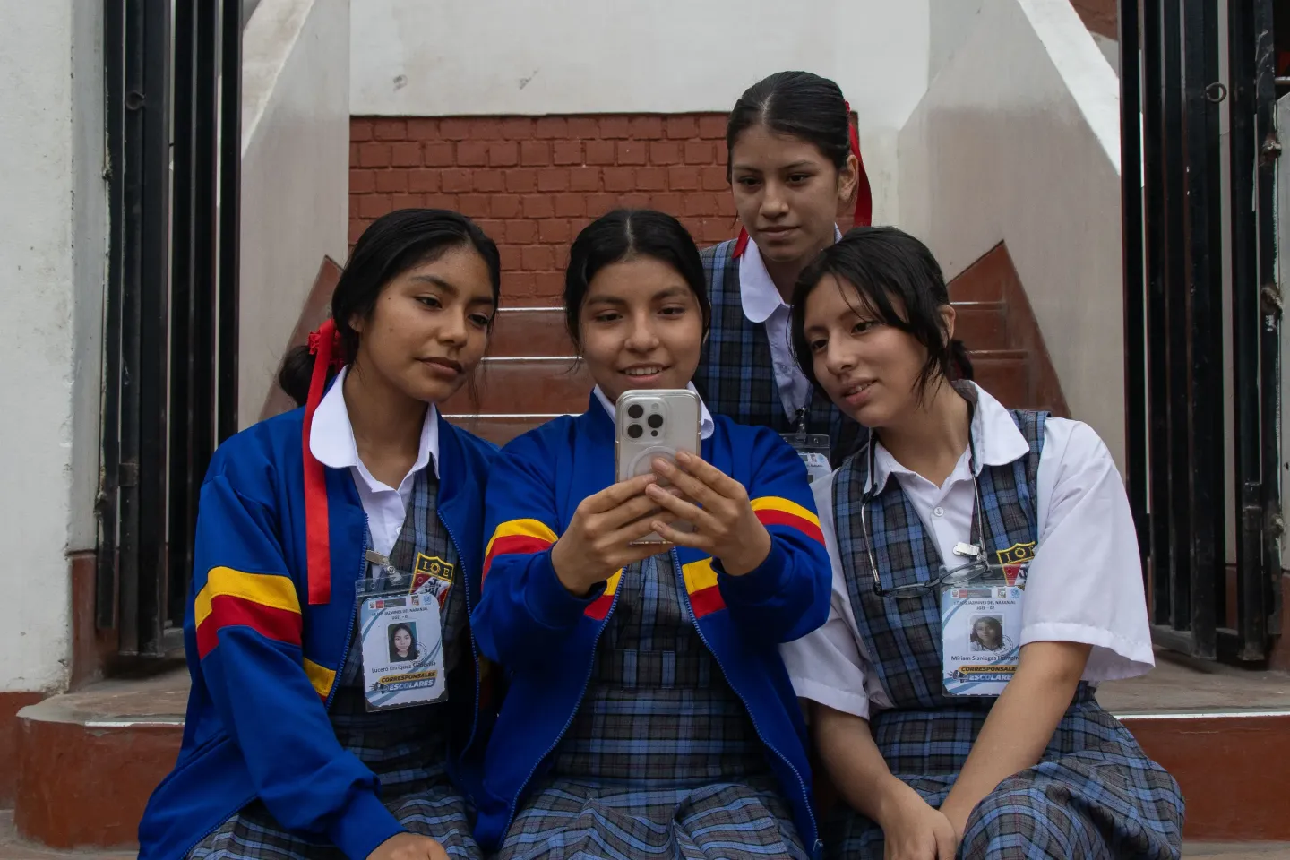 Five teenage girls in school uniform are taking a selfie photo with an Iphone.