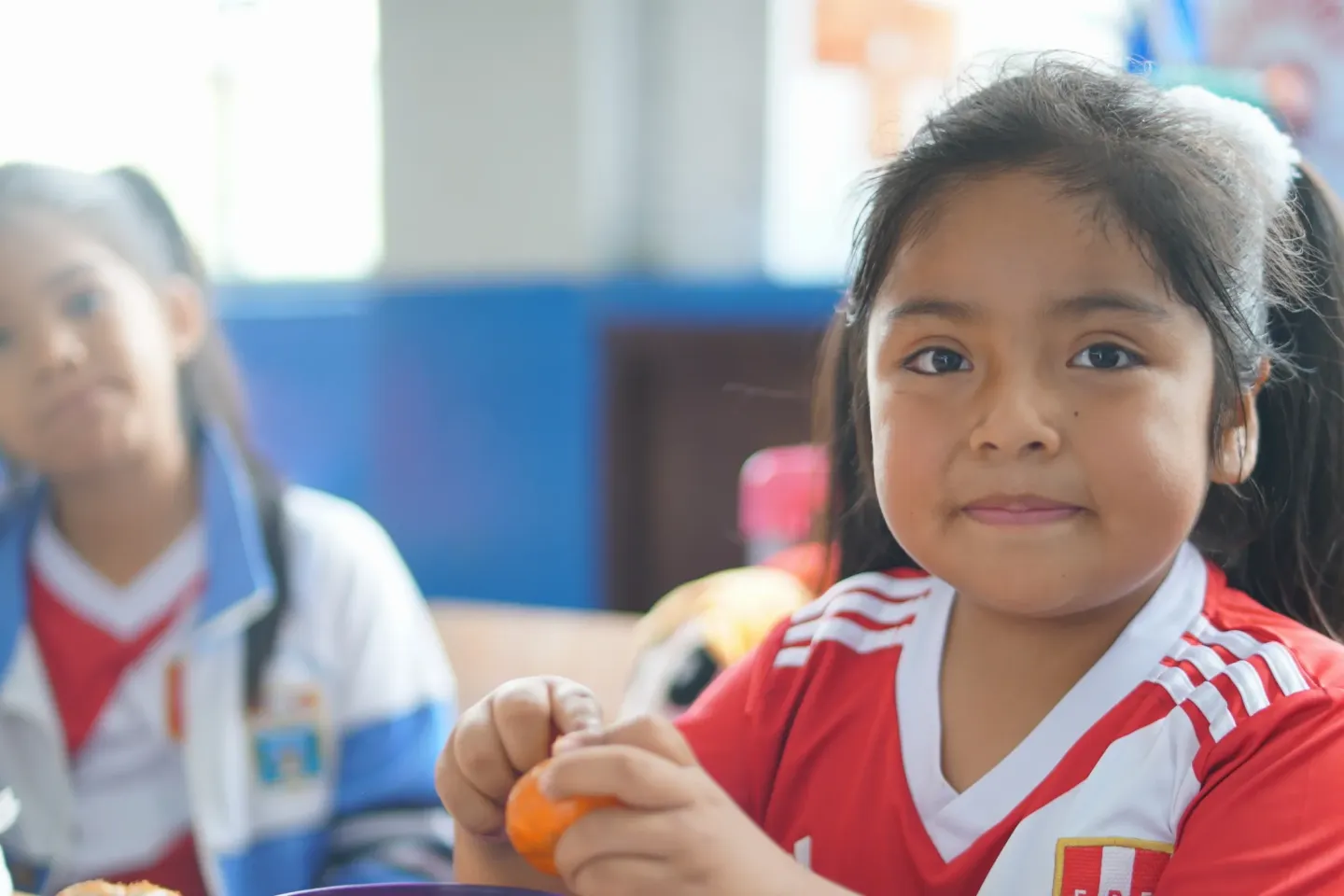 A girl sits in a classroom while eating fruit