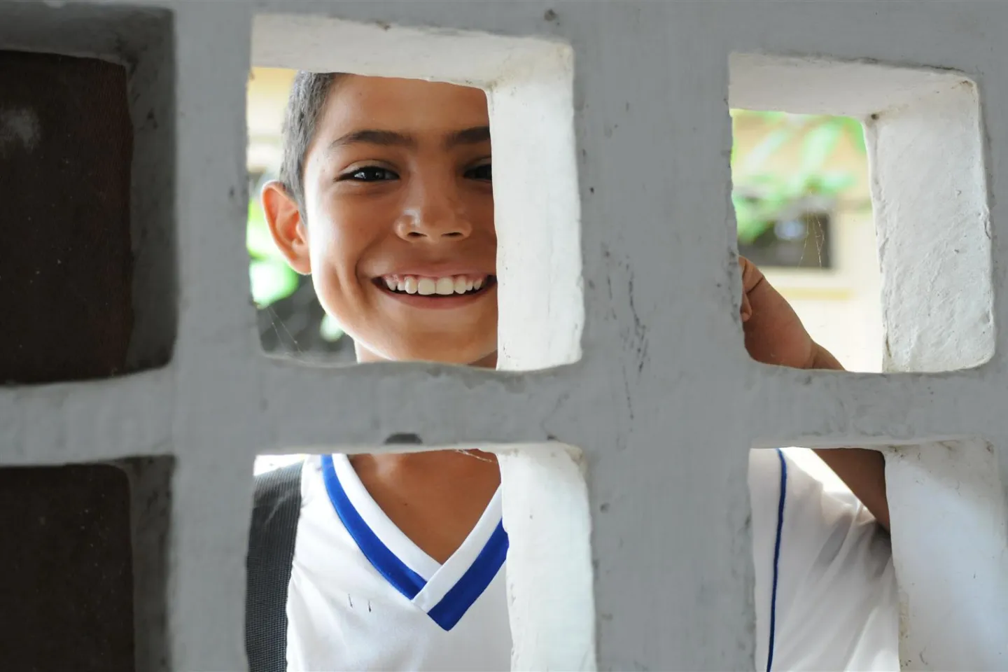 C&eacute;sar, 12, a sixth-grade student, smiles as he peers through a cement block window of a classroom in Colombia