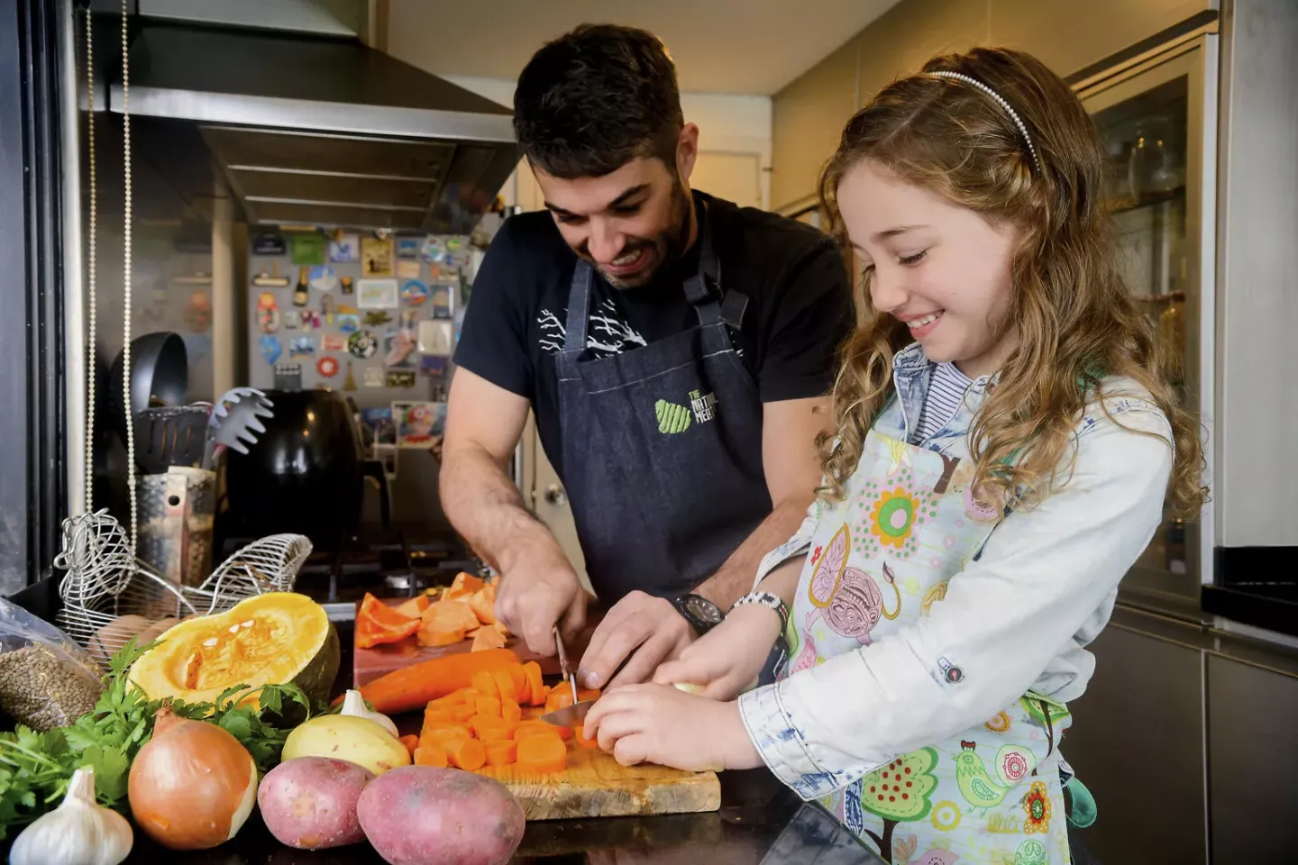 Un hombre adulto, una adolescente y una ni&ntilde;a cortando frutas y verduras en la cocina
