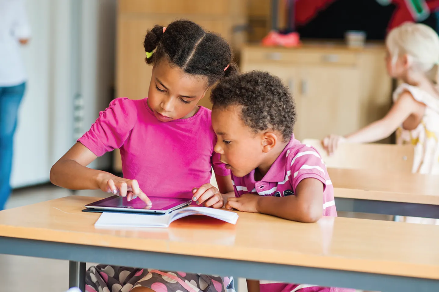 Una ni&ntilde;a y un ni&ntilde;o miran una tablet dentro de un sal&oacute;n de clases