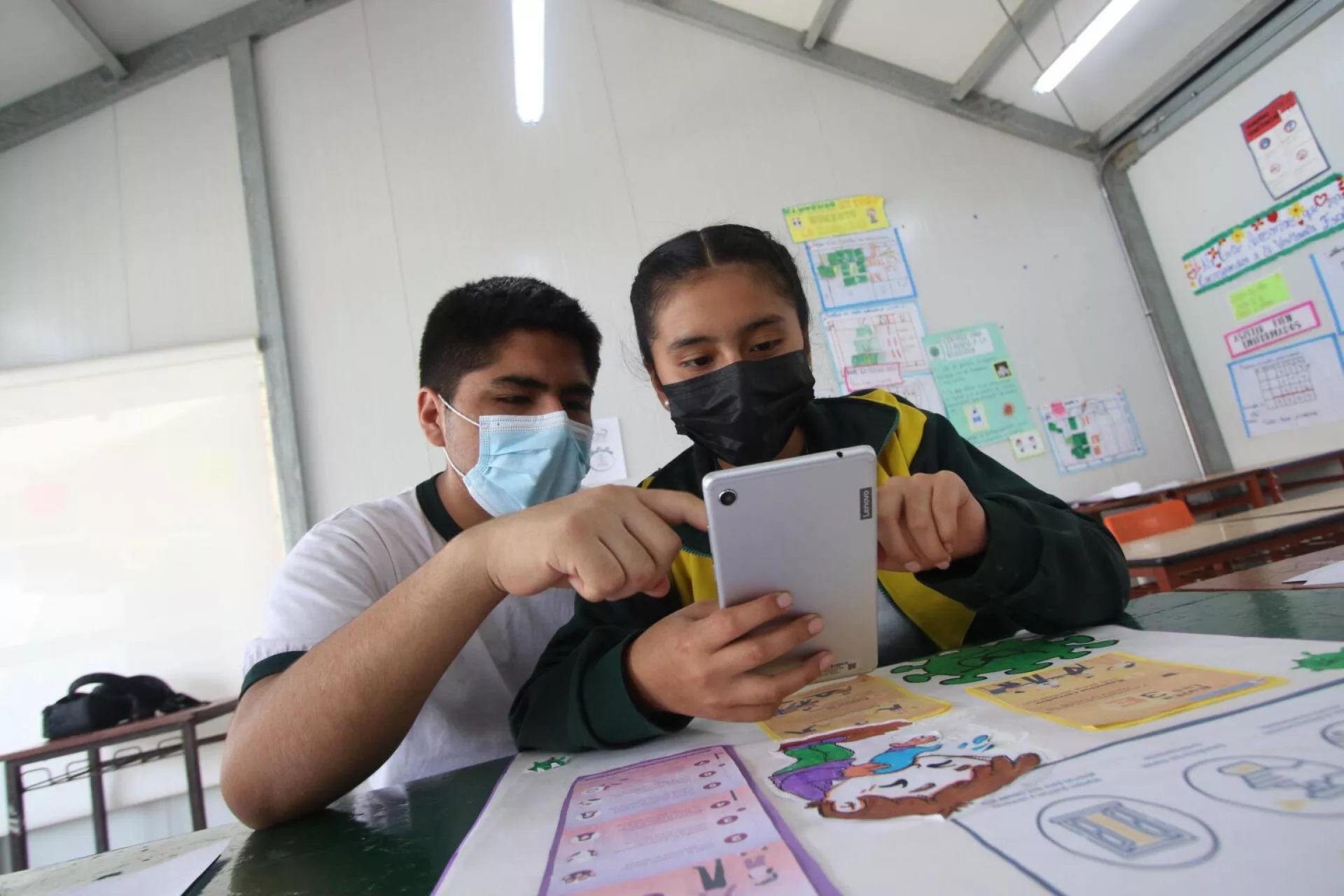 Dos jovenes miran un tablet en el salon de clases