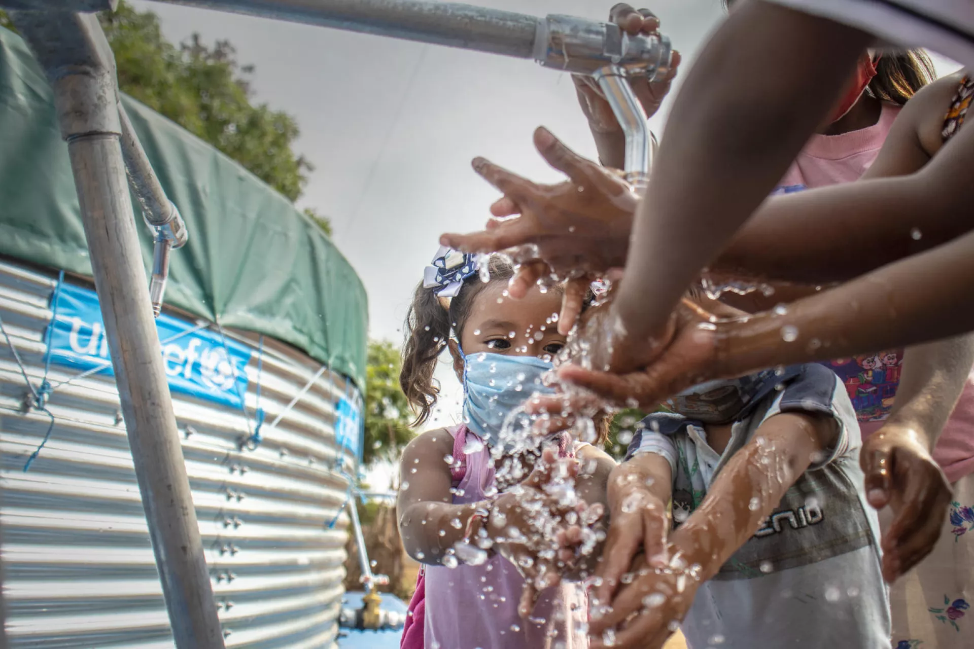 A young girl is washing her hands with other people