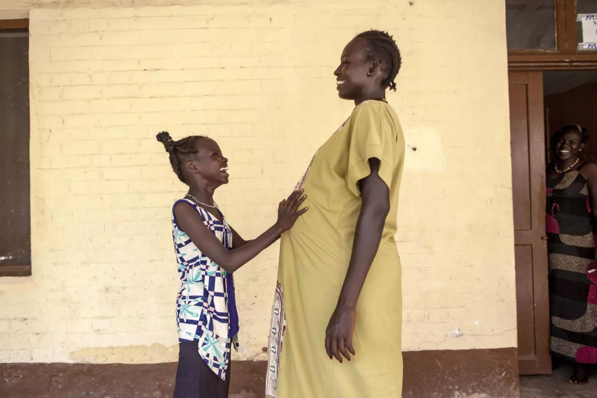 11 year old Nyanyiik Abile touches the stomach of Sundoay John - who is 9 months pregnant with her second child - outside the UNICEF-supported maternity ward at Malakal Teaching Hospital, South Sudan.