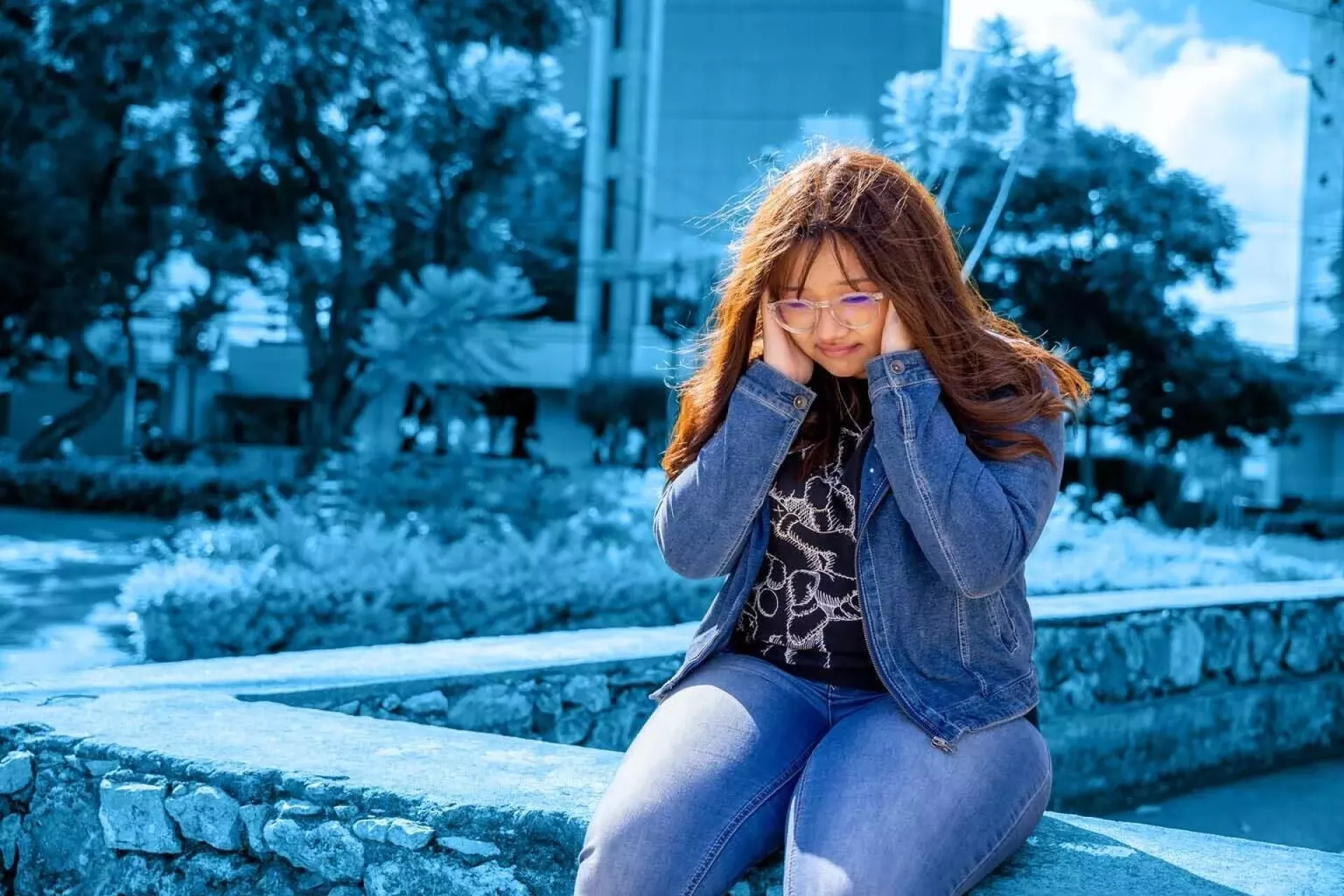 adolescentes sentada sola, tap&aacute;ndose los o&iacute;dos con ambas manos.