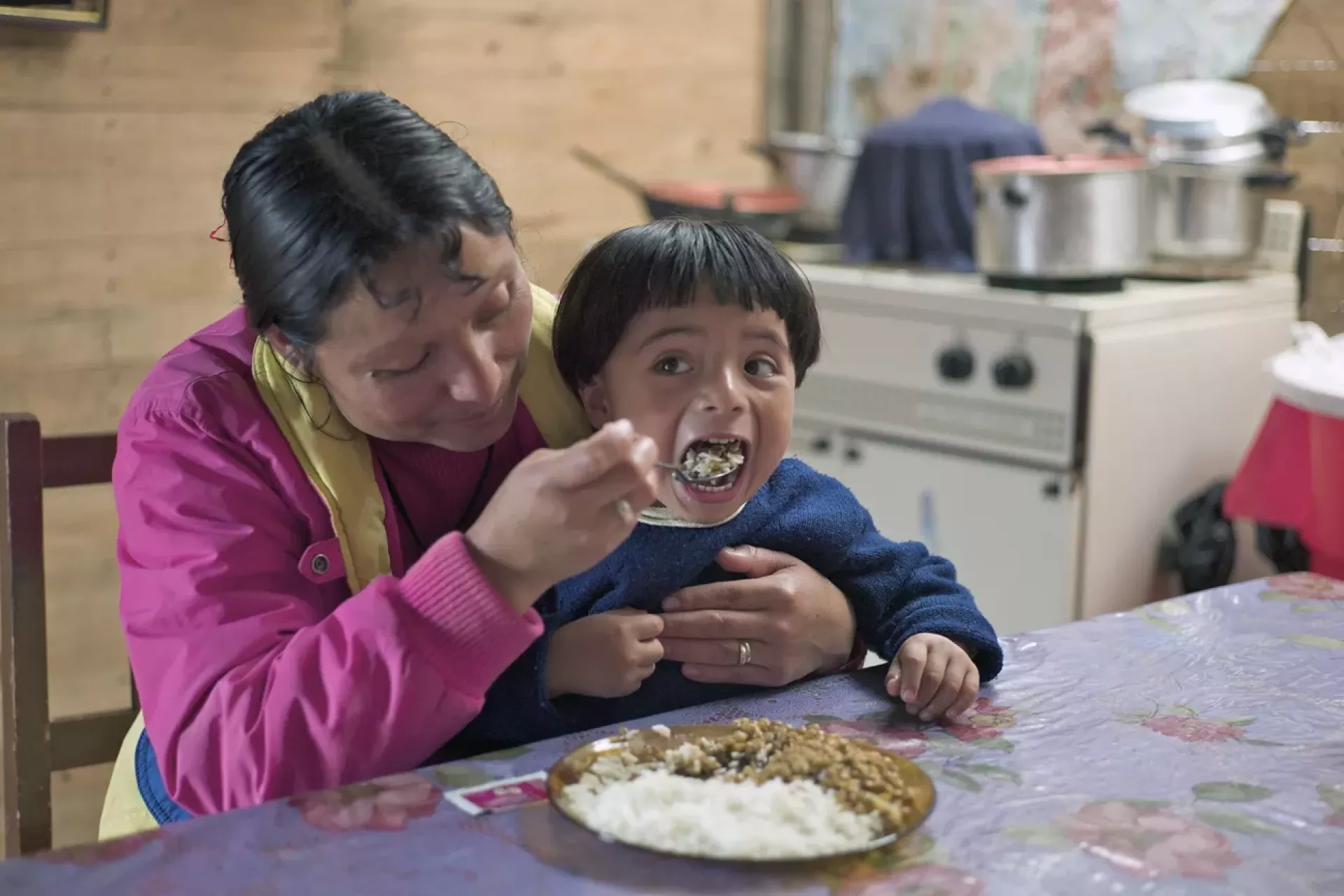 Una madre da de comer a su hijo un plato de lentejas con arroz.