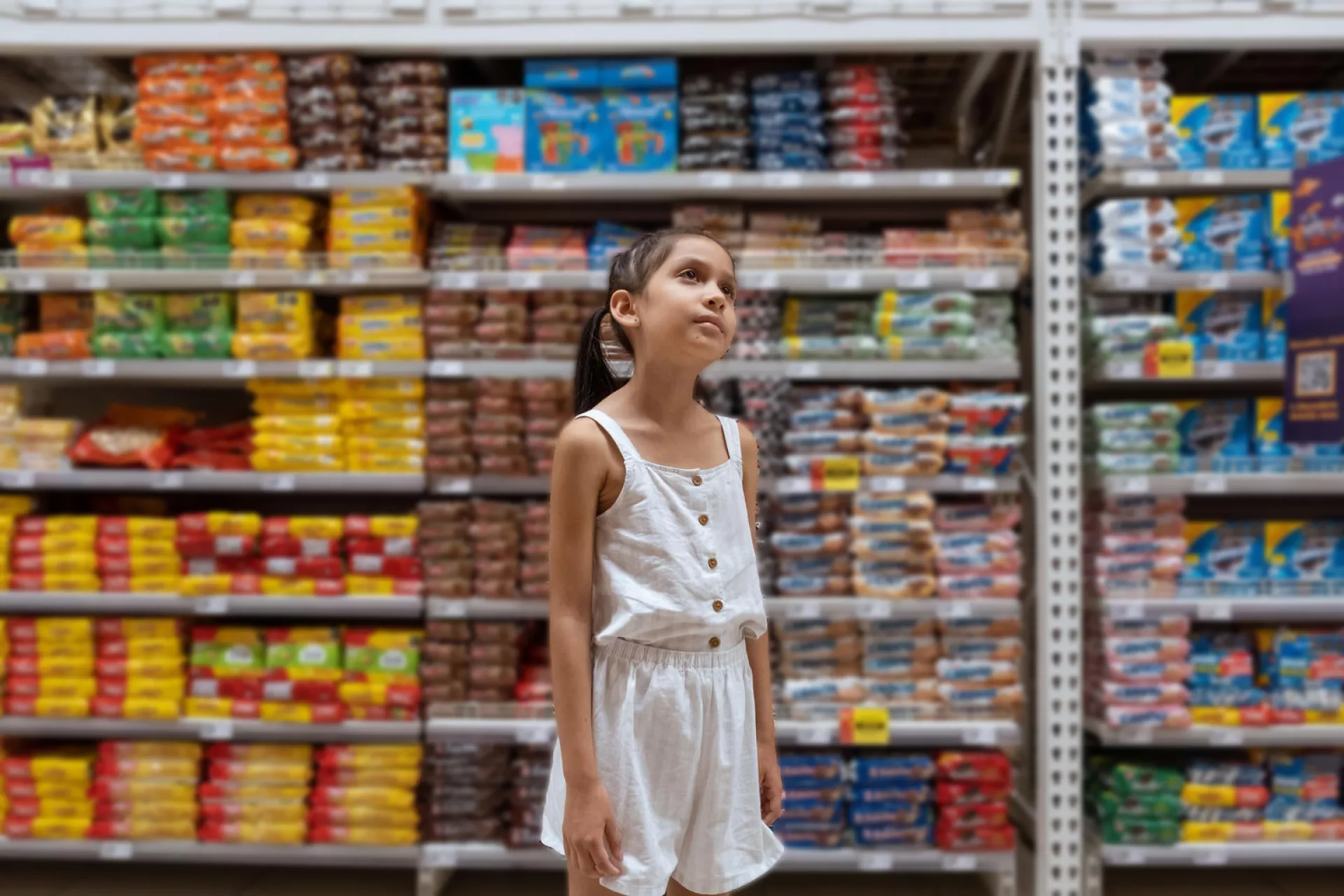 Ni&ntilde;a que est&aacute; parada en medio de estanter&iacute;as de comida chatarra