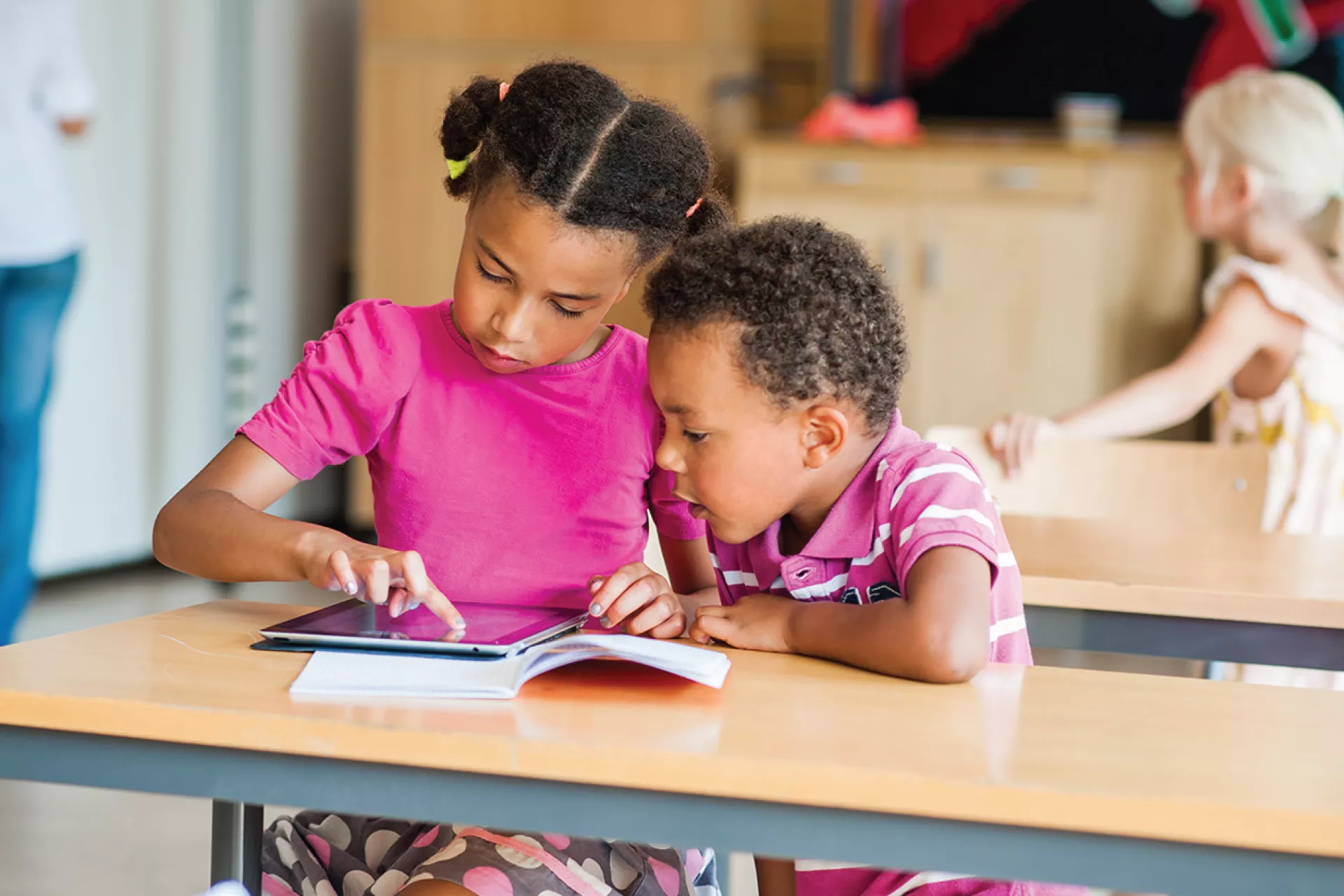 Una ni&ntilde;a y un ni&ntilde;o miran una tablet dentro de un sal&oacute;n de clases
