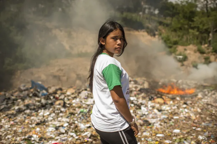 Ni&ntilde;a parada frente a basura incendiada.