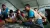 Un hombre sentado habla mientras un grupo de ni&ntilde;os alrededor le presta atenci&oacute;n.